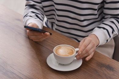 Photo of Woman using smartphone during coffee break at wooden table indoors, closeup