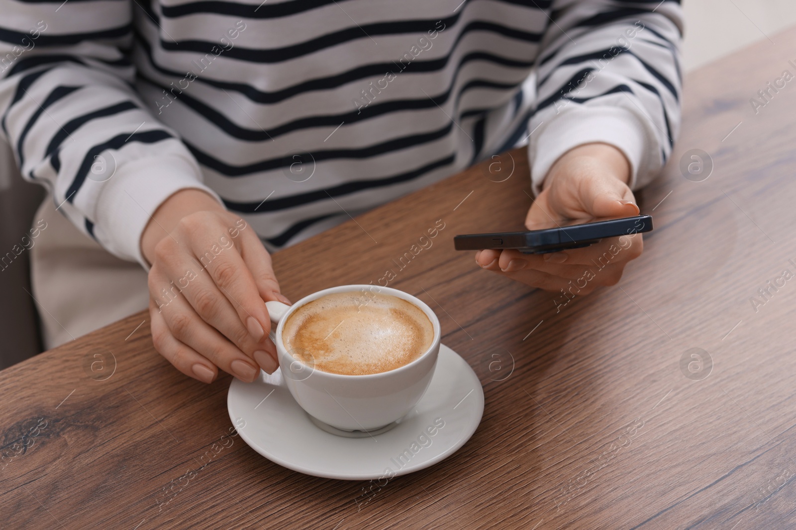 Photo of Woman using smartphone during coffee break at wooden table indoors, closeup