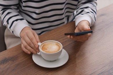 Photo of Woman using smartphone during coffee break at wooden table indoors, closeup