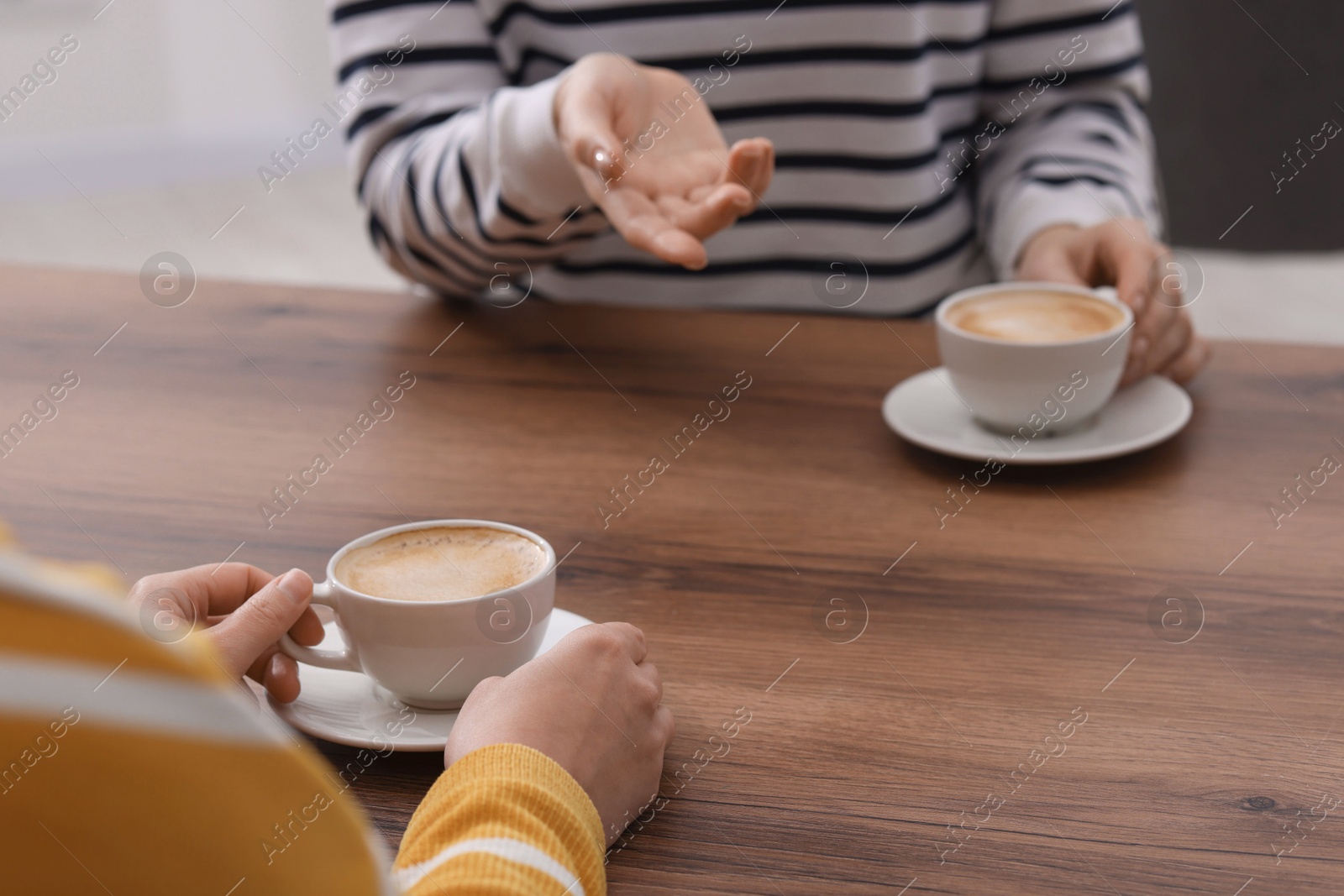 Photo of Coffee break. Women with cups of hot drinks at wooden table indoors, closeup