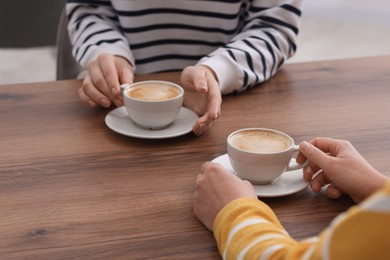 Photo of Coffee break. Women with cups of hot drinks at wooden table indoors, closeup