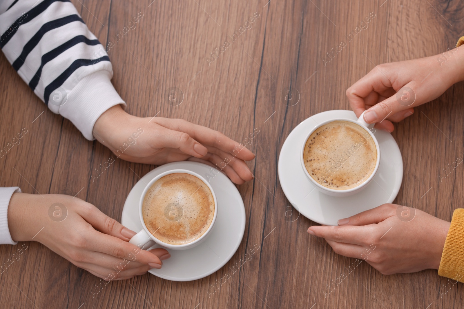 Photo of Coffee break. Women with cups of hot drinks at wooden table, top view