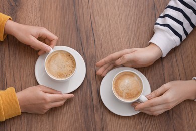 Photo of Coffee break. Women with cups of hot drinks at wooden table, top view