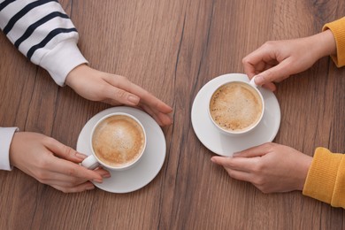 Photo of Coffee break. Women with cups of hot drinks at wooden table, top view