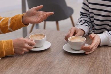 Photo of Coffee break. Women with cups of hot drinks at wooden table indoors, closeup