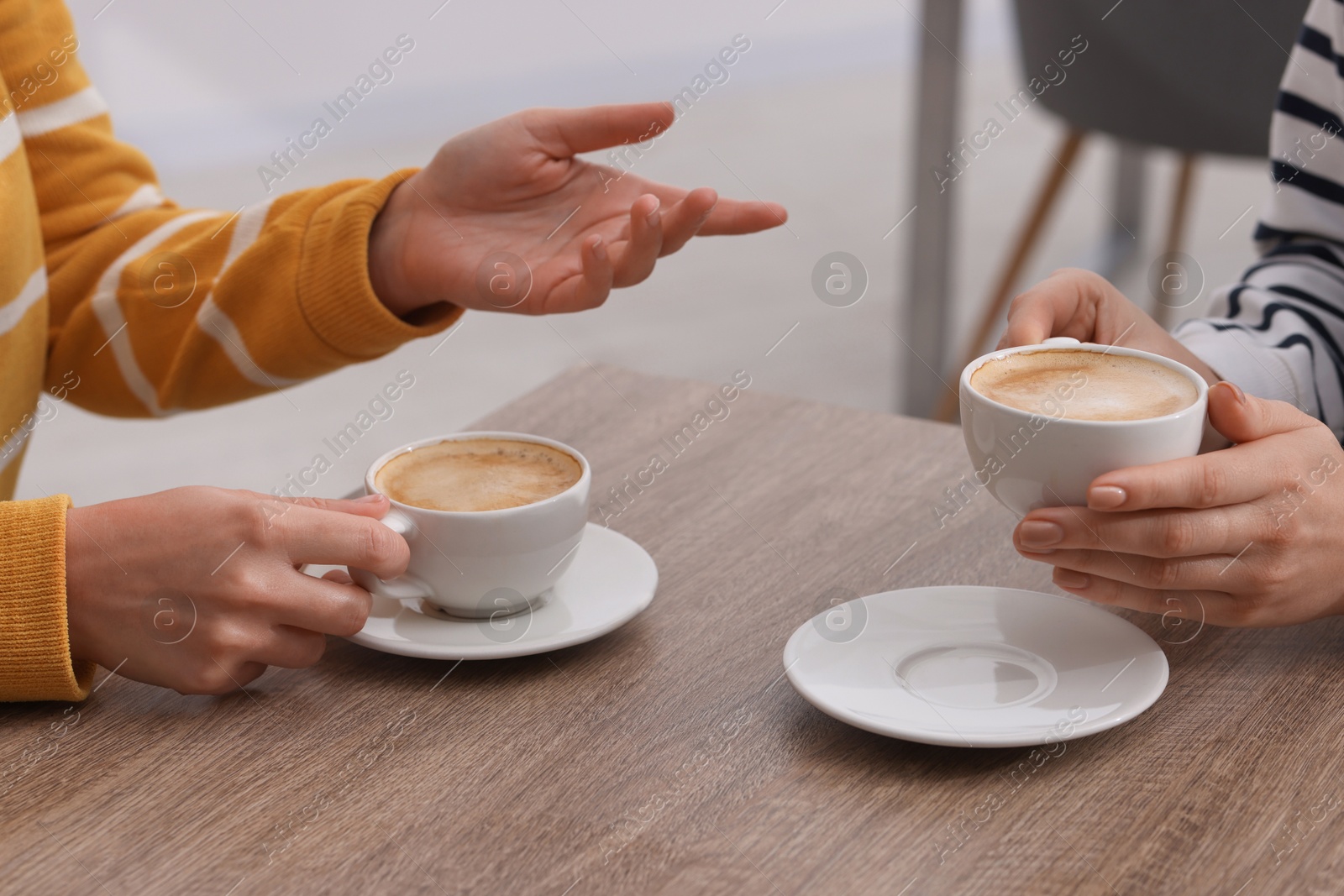 Photo of Coffee break. Women with cups of hot drinks at wooden table indoors, closeup