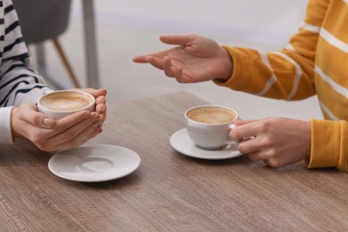 Photo of Coffee break. Women with cups of hot drinks at wooden table indoors, closeup