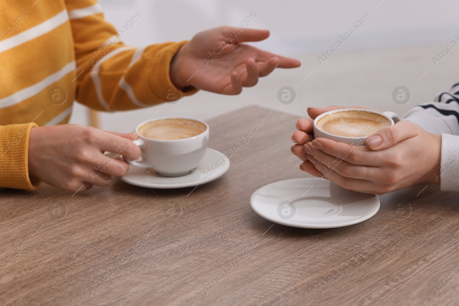 Photo of Coffee break. Women with cups of hot drinks at wooden table indoors, closeup