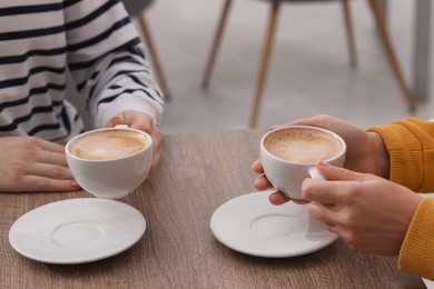 Photo of Coffee break. Women with cups of hot drinks at wooden table indoors, closeup