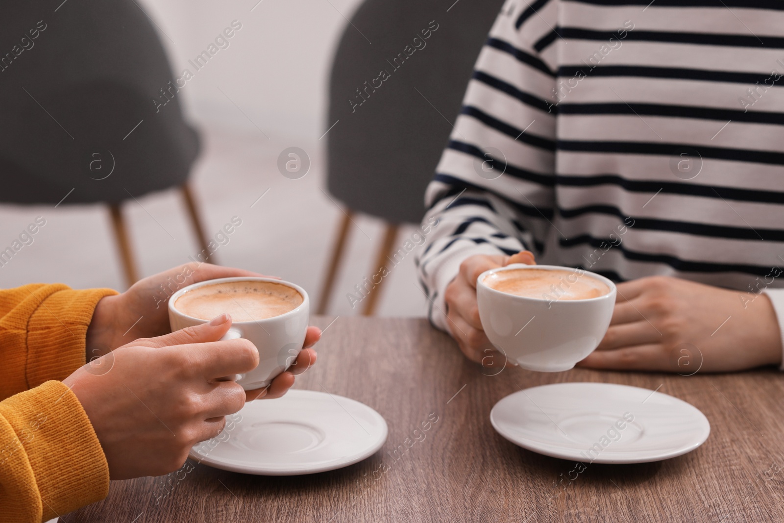 Photo of Coffee break. Women with cups of hot drinks at wooden table indoors, closeup