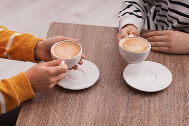 Photo of Coffee break. Women with cups of hot drinks at wooden table indoors, closeup