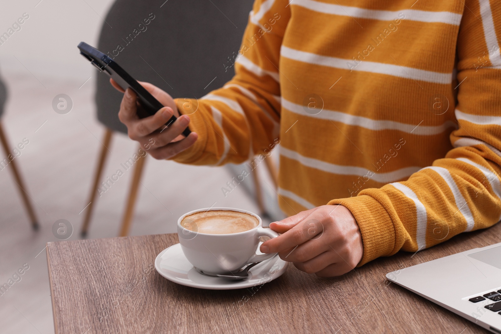 Photo of Woman using smartphone during coffee break at wooden table indoors, closeup