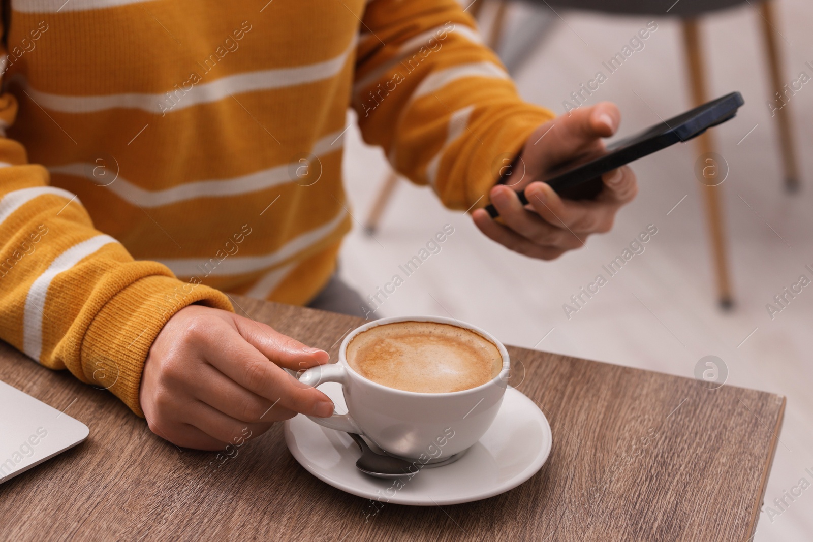 Photo of Woman using smartphone during coffee break at wooden table indoors, closeup