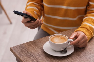 Photo of Woman using smartphone during coffee break at wooden table indoors, closeup