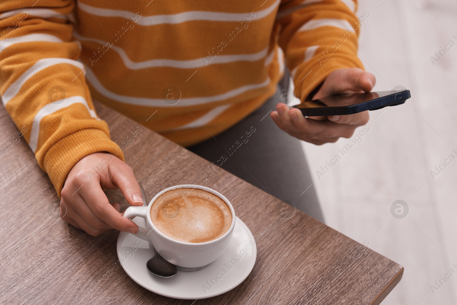 Photo of Woman using smartphone during coffee break at wooden table indoors, closeup