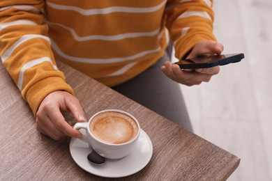 Photo of Woman using smartphone during coffee break at wooden table indoors, closeup