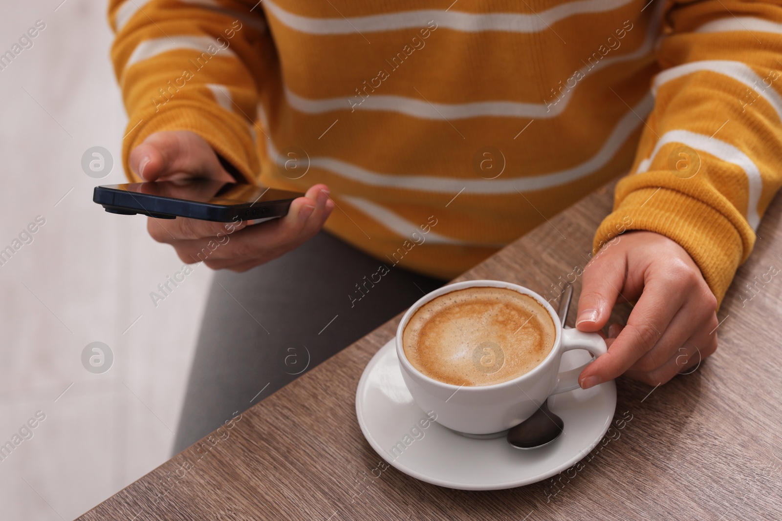 Photo of Woman using smartphone during coffee break at wooden table indoors, closeup