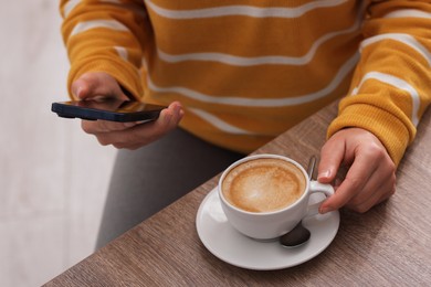 Photo of Woman using smartphone during coffee break at wooden table indoors, closeup