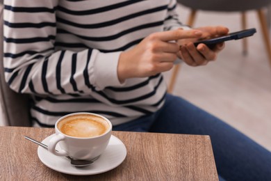 Photo of Woman using smartphone during coffee break at wooden table indoors, closeup