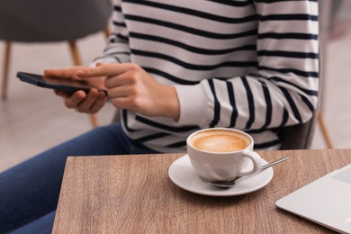 Photo of Woman using smartphone during coffee break at wooden table indoors, closeup