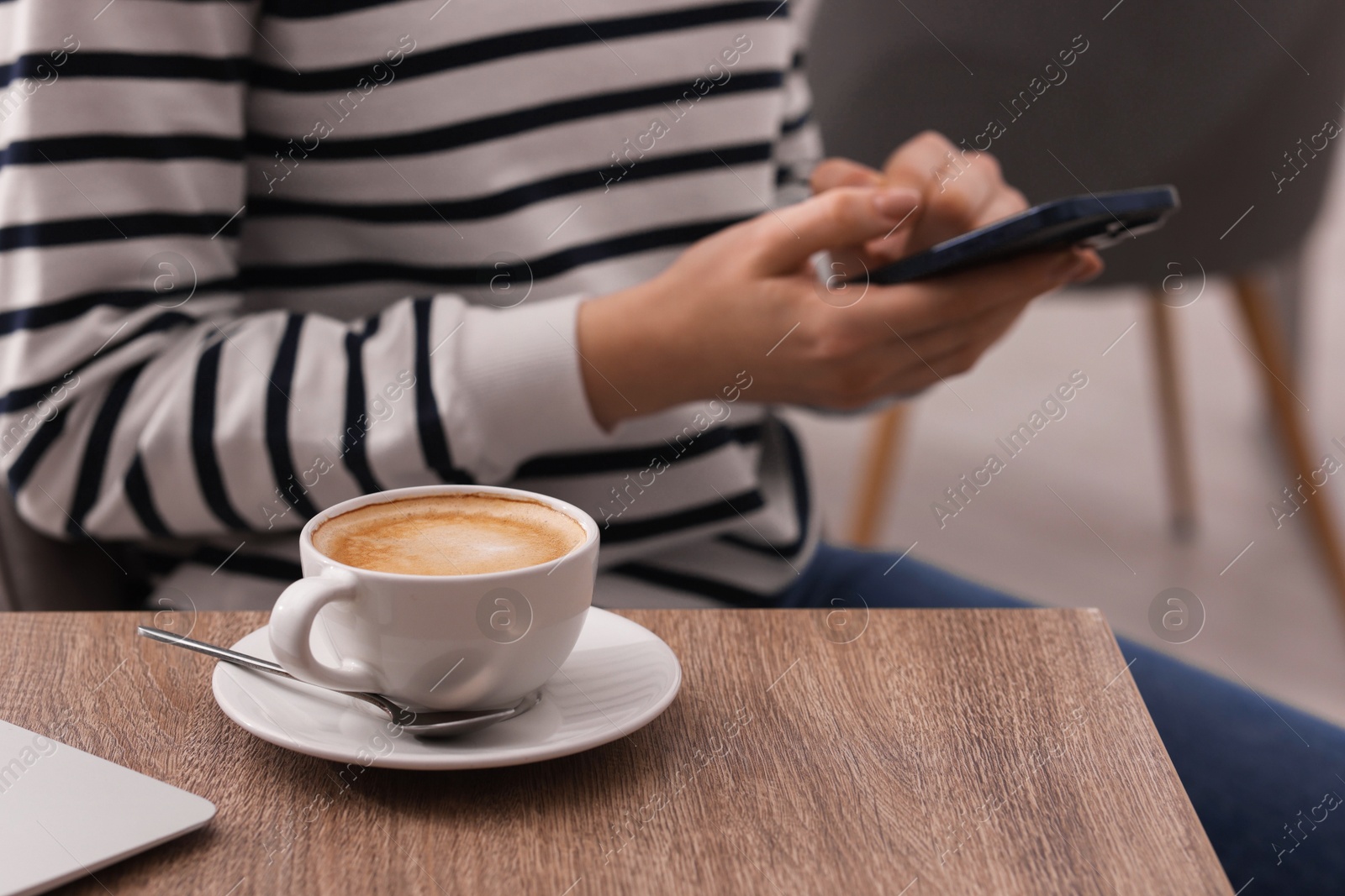 Photo of Woman using smartphone during coffee break at wooden table indoors, closeup