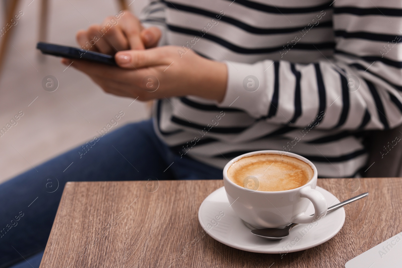 Photo of Woman using smartphone during coffee break at wooden table indoors, closeup