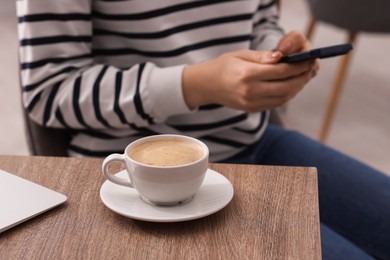 Photo of Woman using smartphone during coffee break at wooden table indoors, closeup