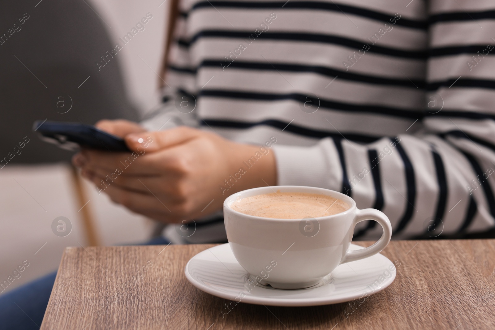 Photo of Woman using smartphone during coffee break at wooden table indoors, closeup