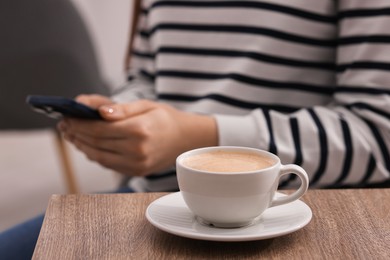 Photo of Woman using smartphone during coffee break at wooden table indoors, closeup