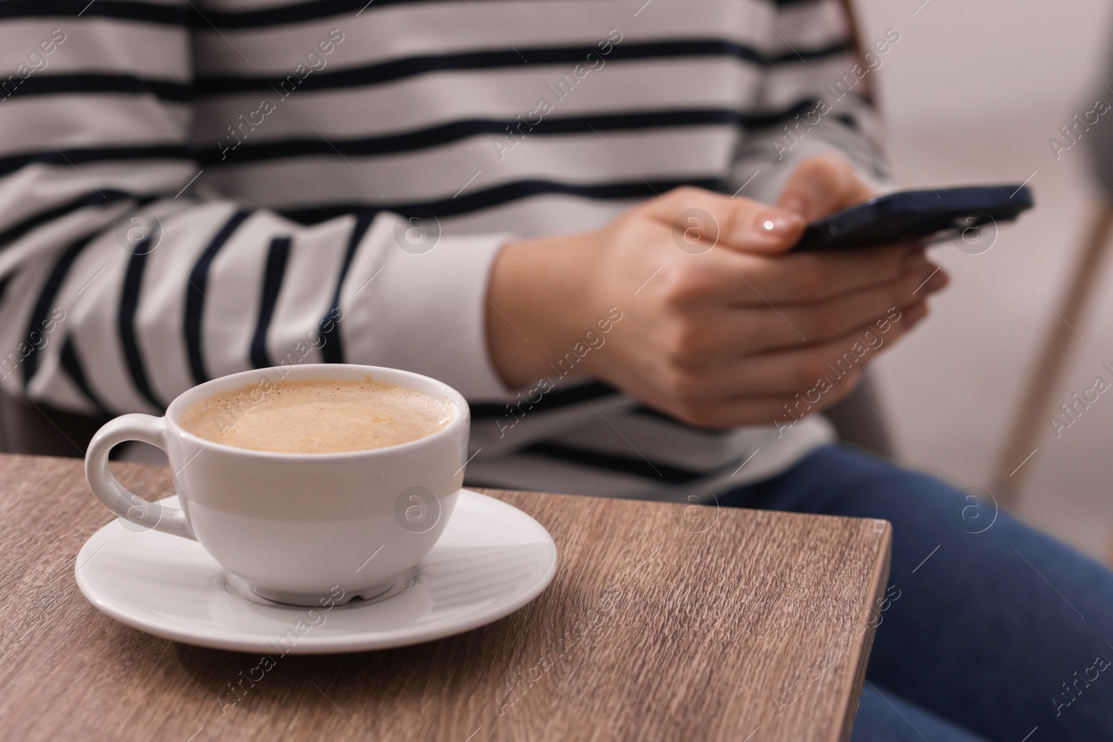 Photo of Woman using smartphone during coffee break at wooden table indoors, closeup