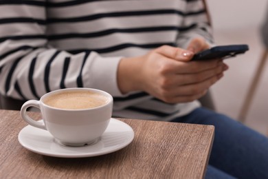 Photo of Woman using smartphone during coffee break at wooden table indoors, closeup