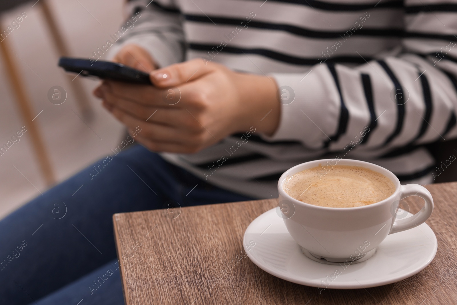 Photo of Woman using smartphone during coffee break at wooden table indoors, closeup