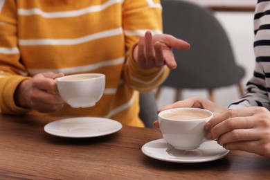 Photo of Coffee break. Women with cups of hot drinks at wooden table indoors, closeup