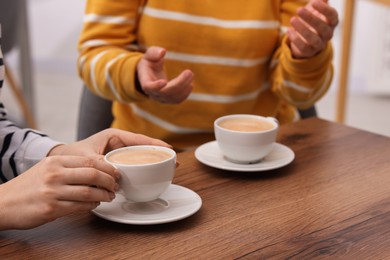 Photo of Coffee break. Women with cups of hot drinks at wooden table indoors, closeup