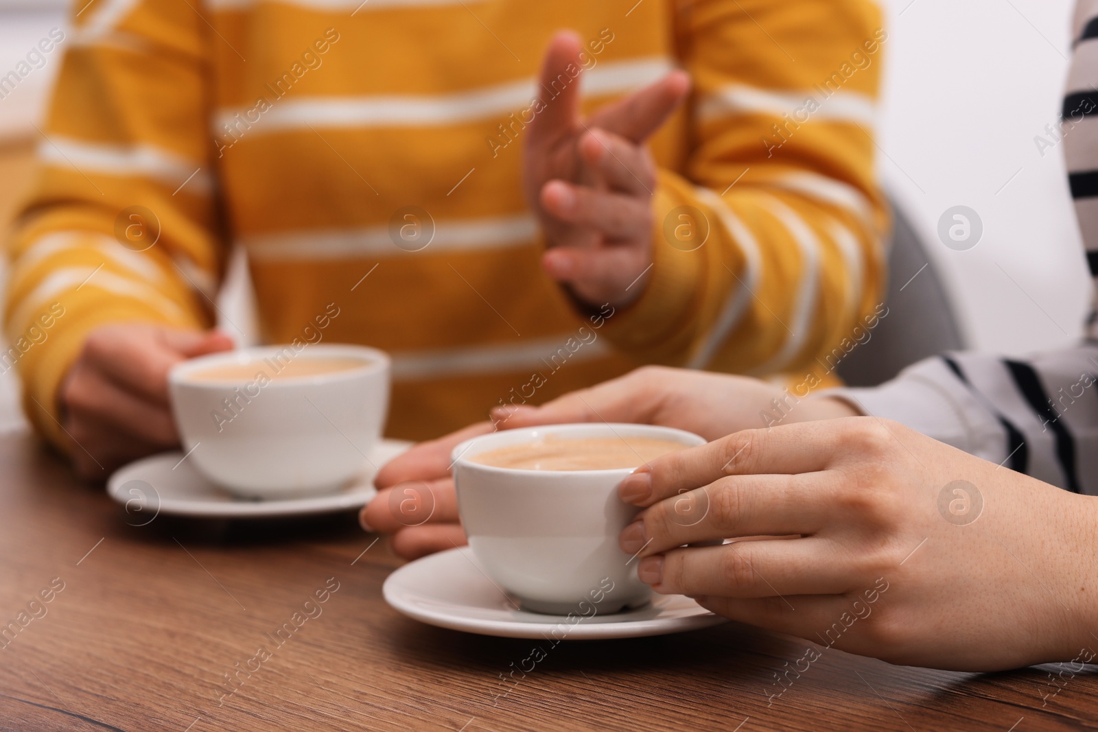 Photo of Coffee break. Women with cups of hot drinks at wooden table indoors, closeup