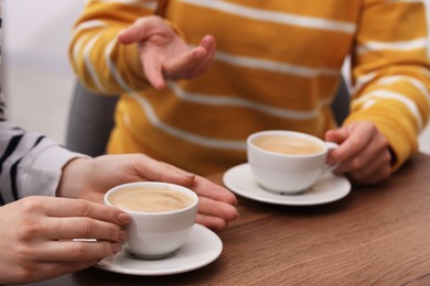 Photo of Coffee break. Women with cups of hot drinks at wooden table indoors, closeup