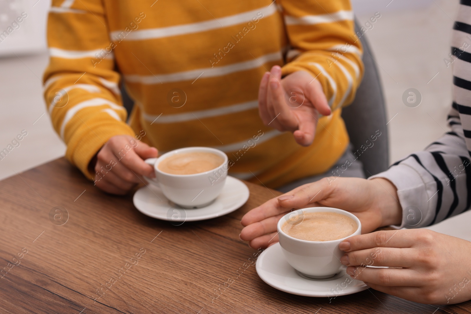 Photo of Coffee break. Women with cups of hot drinks at wooden table indoors, closeup