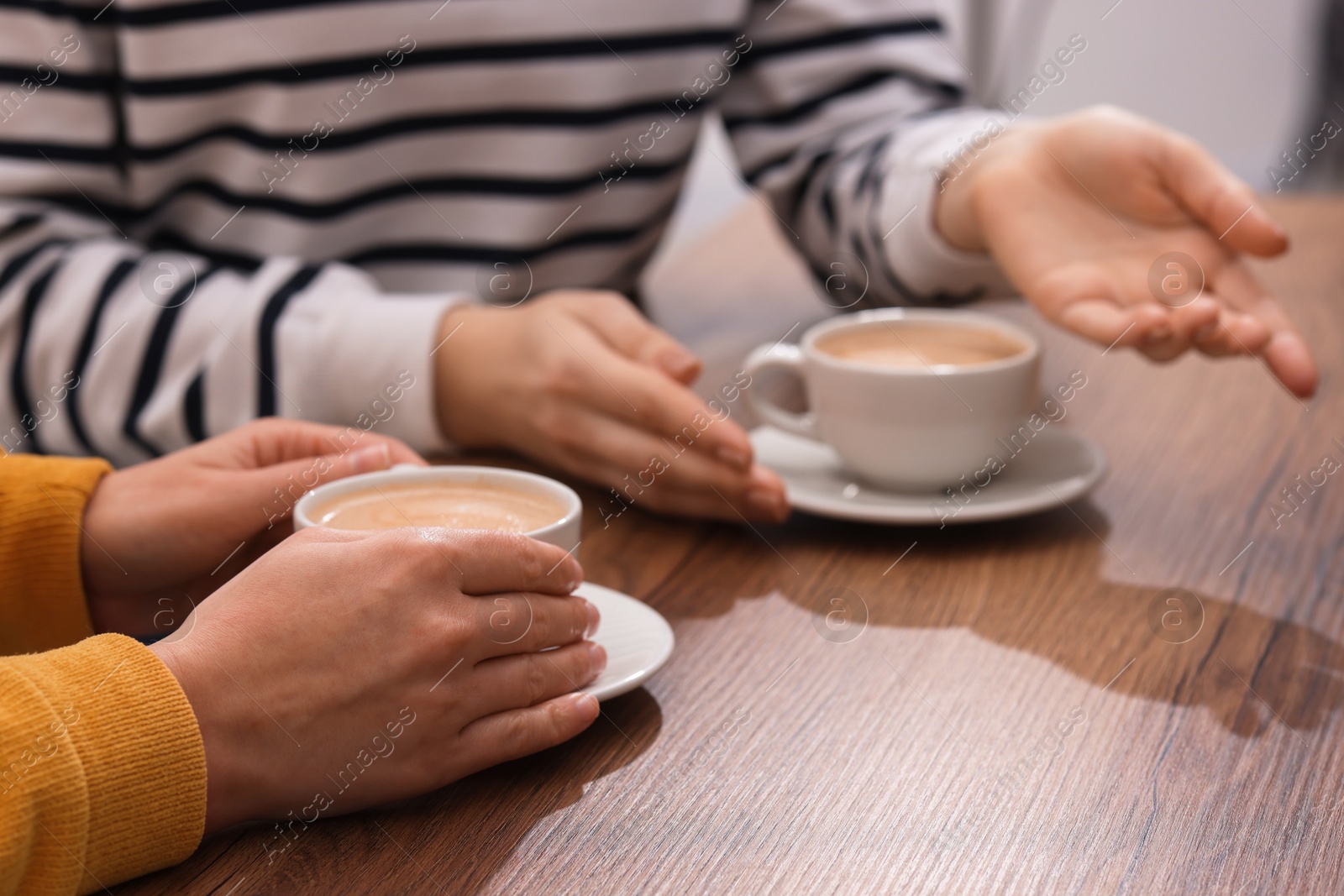 Photo of Coffee break. Women with cups of hot drinks at wooden table indoors, closeup