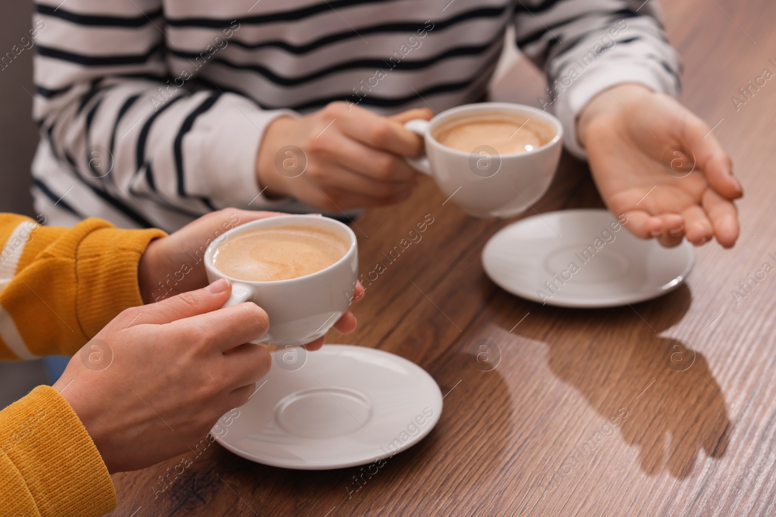 Photo of Coffee break. Women with cups of hot drinks at wooden table indoors, closeup