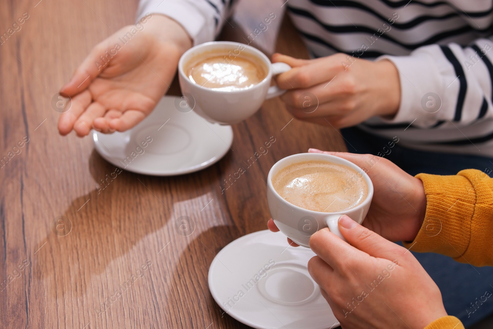 Photo of Coffee break. Women with cups of hot drinks at wooden table indoors, closeup