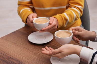 Photo of Coffee break. Women with cups of hot drinks at wooden table indoors, closeup