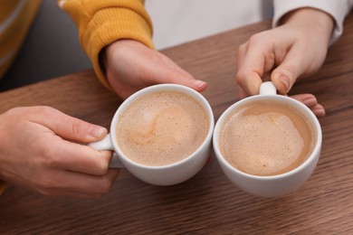 Photo of Coffee break. Women with cups of hot drinks at wooden table indoors, closeup