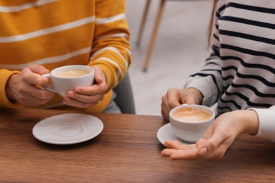 Photo of Coffee break. Women with cups of hot drinks at wooden table indoors, closeup