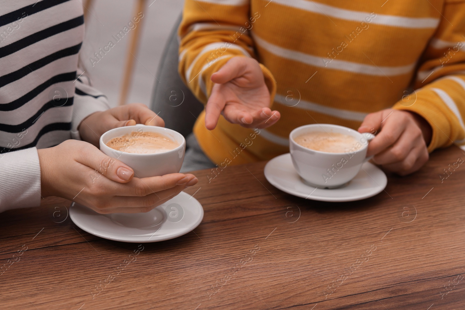 Photo of Coffee break. Women with cups of hot drinks at wooden table indoors, closeup