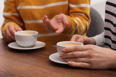 Photo of Coffee break. Women with cups of hot drinks at wooden table indoors, closeup