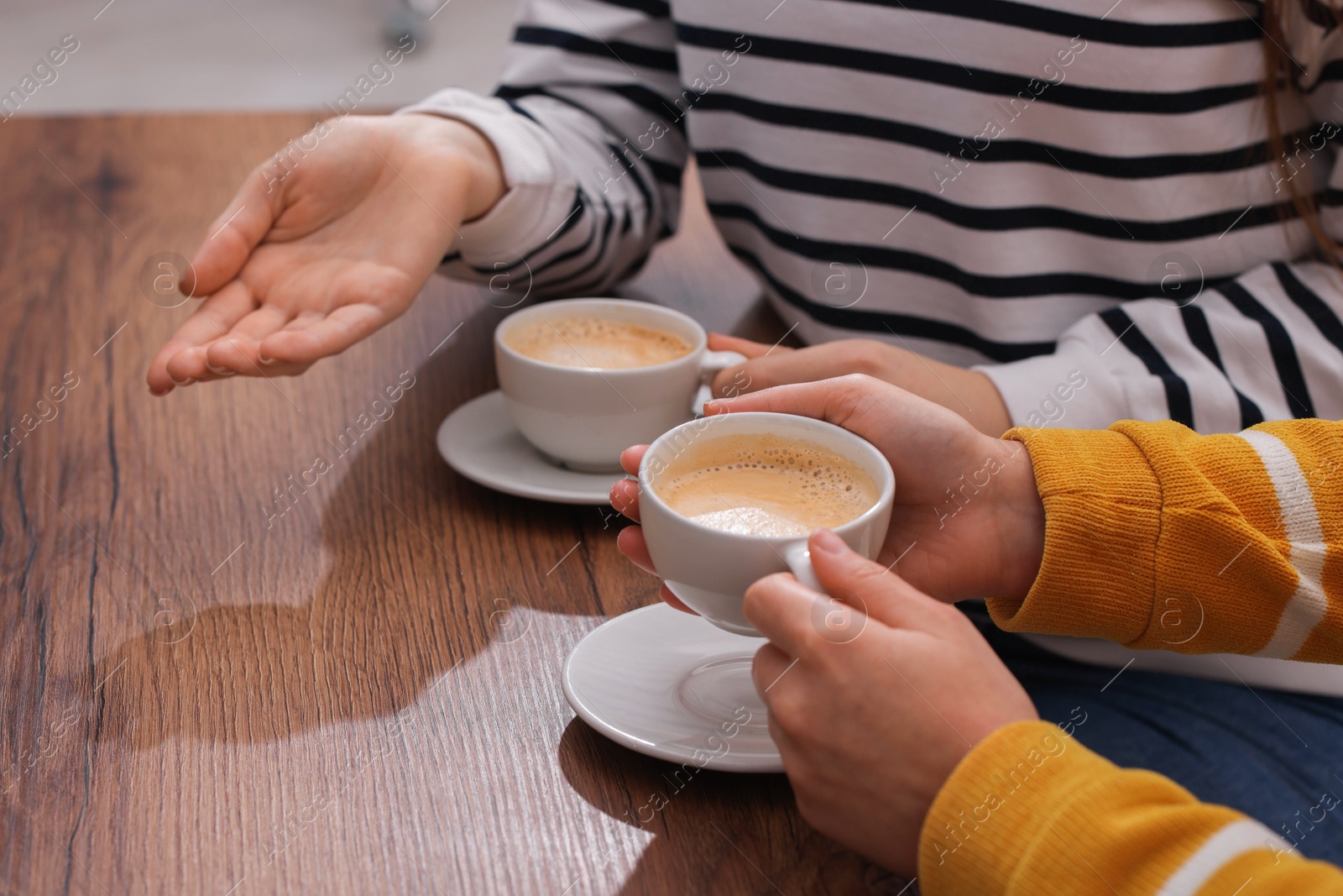 Photo of Coffee break. Women with cups of hot drinks at wooden table indoors, closeup