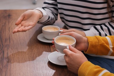 Photo of Coffee break. Women with cups of hot drinks at wooden table indoors, closeup