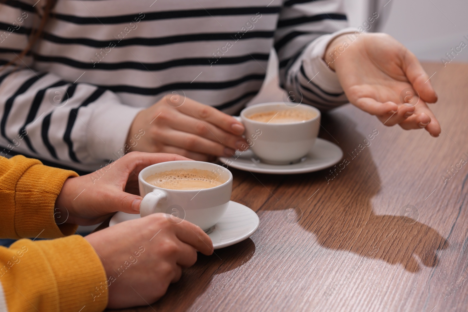 Photo of Coffee break. Women with cups of hot drinks at wooden table indoors, closeup