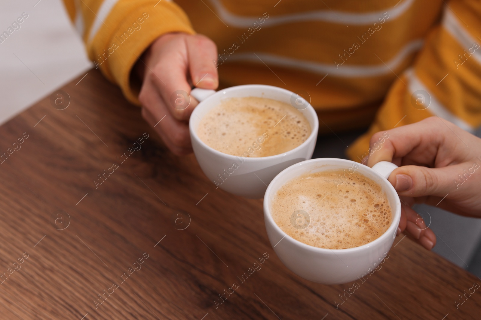 Photo of Coffee break. Women with cups of hot drinks at wooden table indoors, closeup