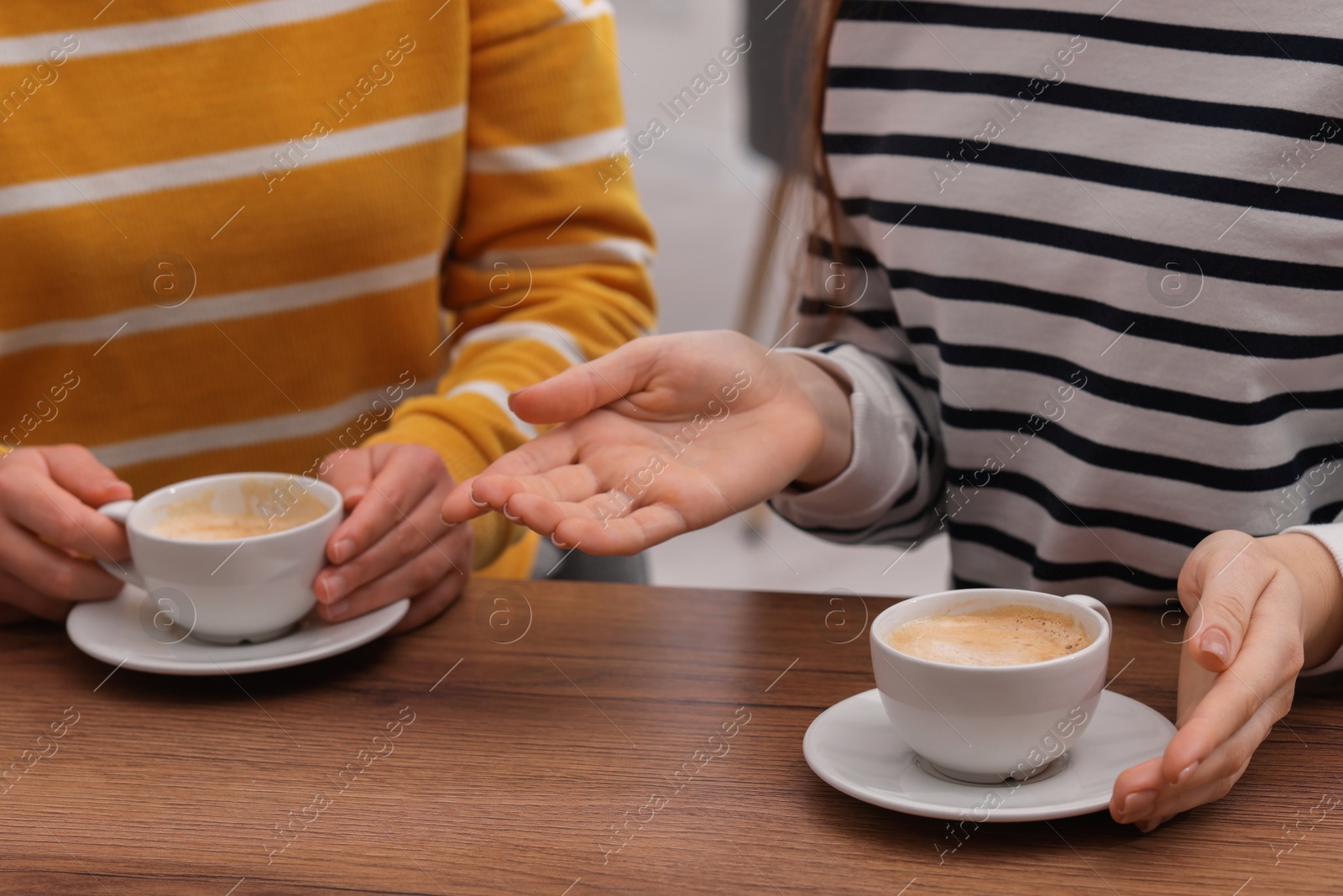 Photo of Coffee break. Women with cups of hot drinks at wooden table indoors, closeup